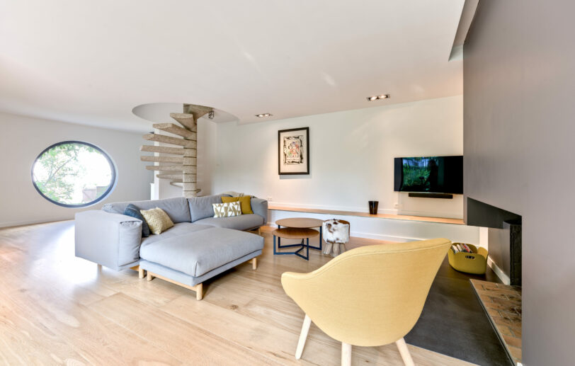 Salon contemporain avec cheminée centrale et touches de couleur chaleureuses – Réalisation d’intérieur par Mise en Scène